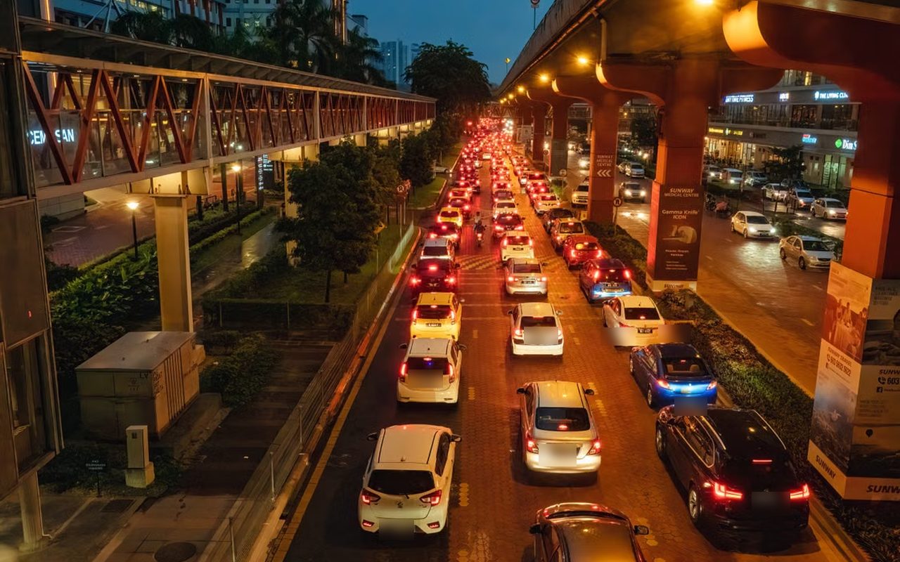 Evening traffic queued in lanes on a Malaysian city road beneath an elevated rail line
