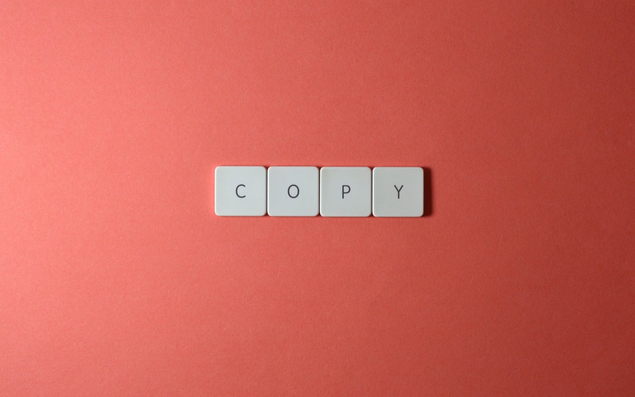 Keyboard letter tiles spelling COPY on a plain coral surface