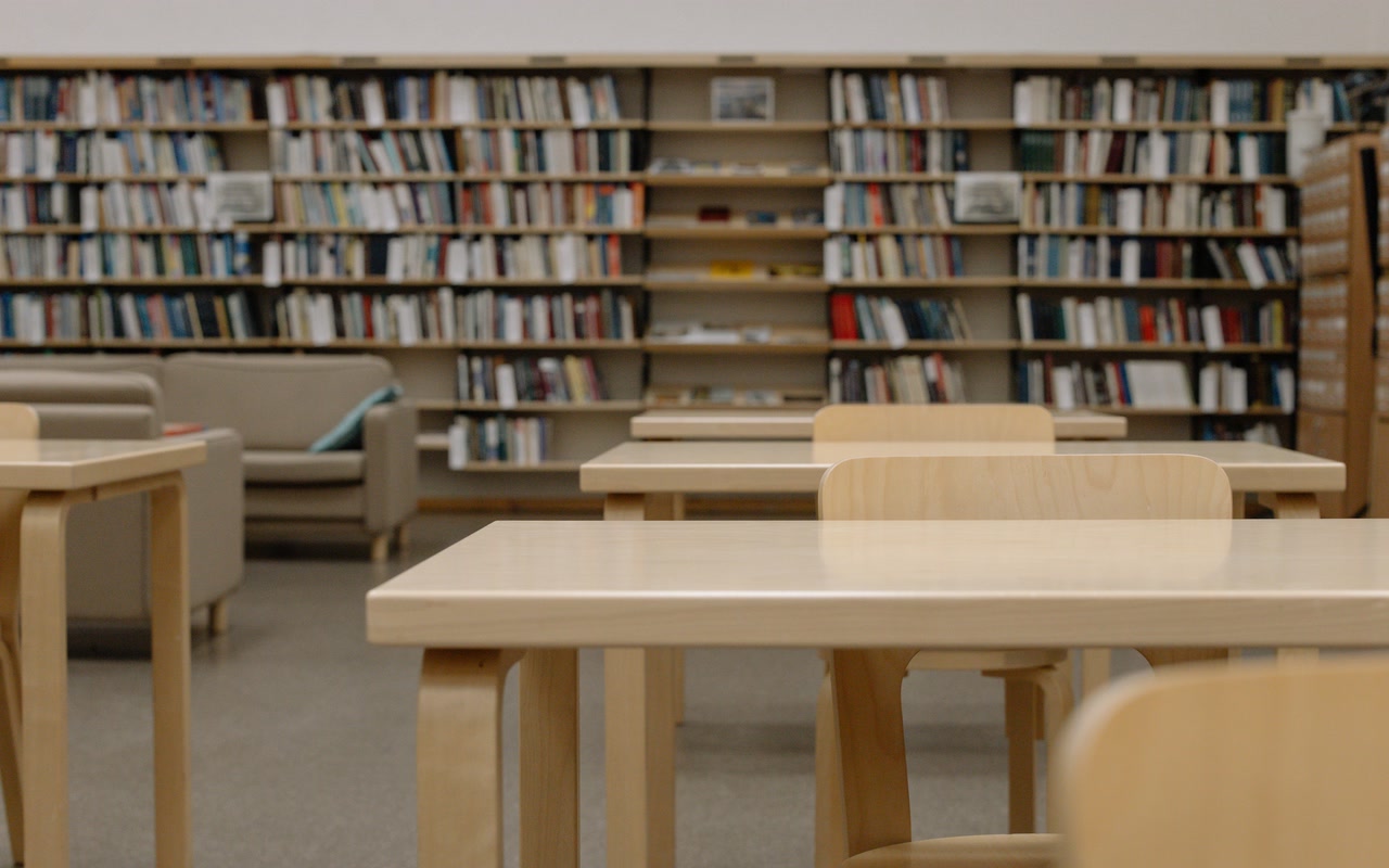 Empty modern university library with wooden study tables, chairs and bookshelves