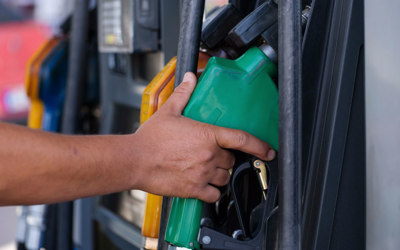 Close-up of a hand holding a green fuel nozzle at an outdoor petrol station