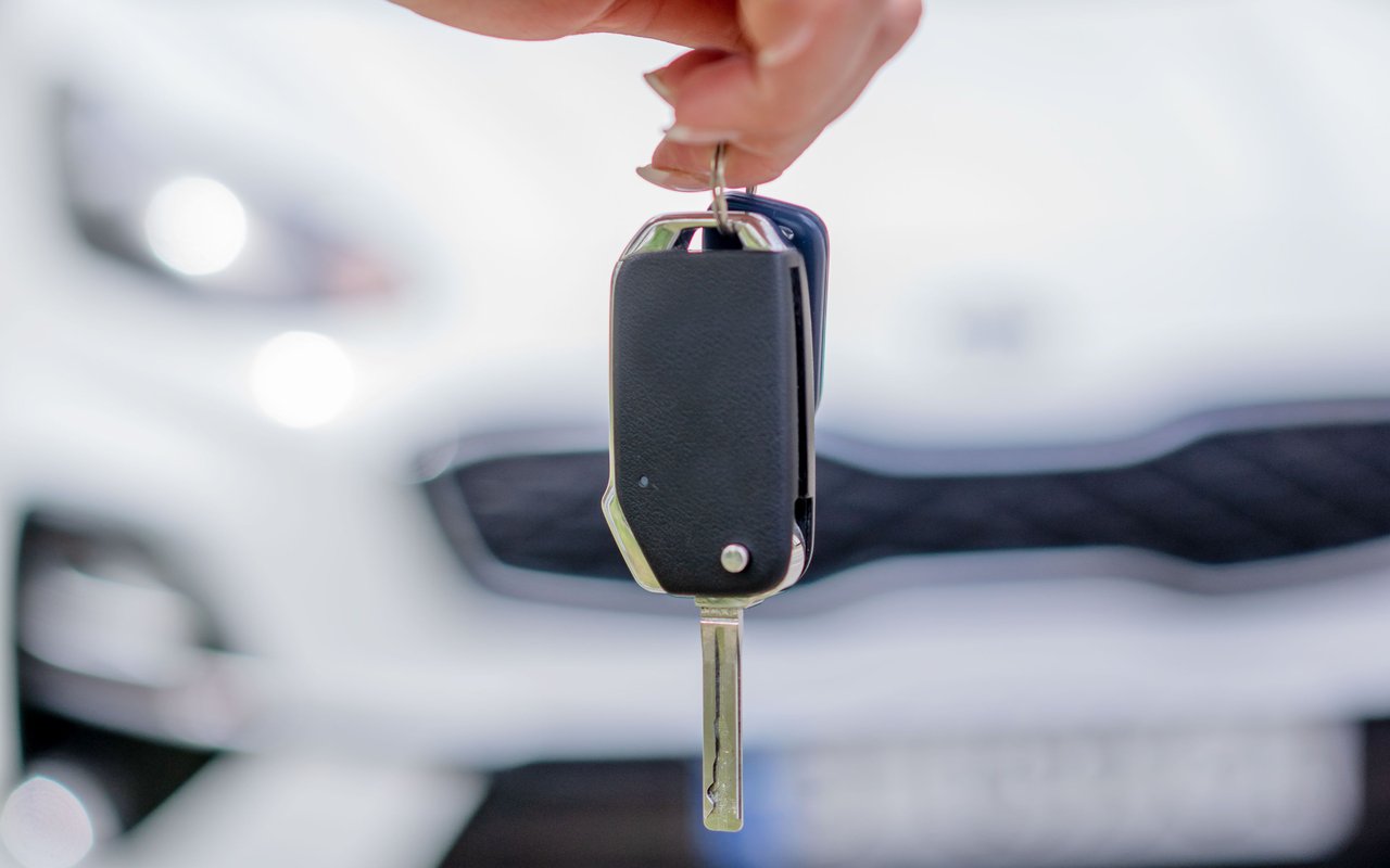 Hand holding a car key in front of a blurred white car