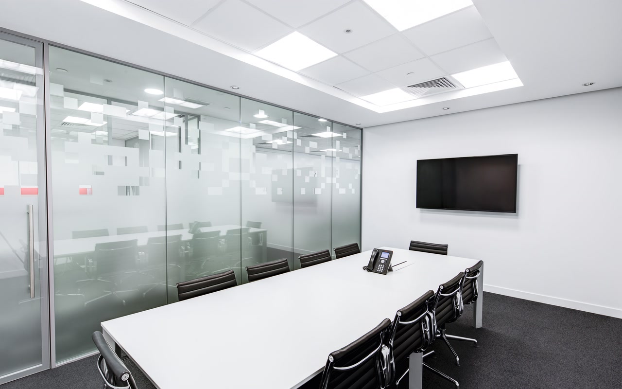Empty glass-walled conference room with a long white table and black office chairs