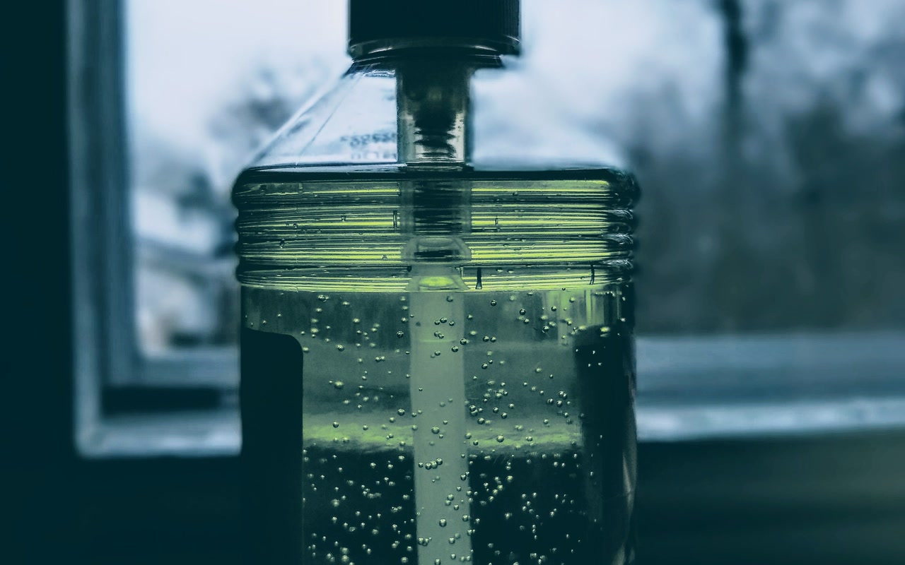 Clear pump bottle of hand sanitiser beside a bright window