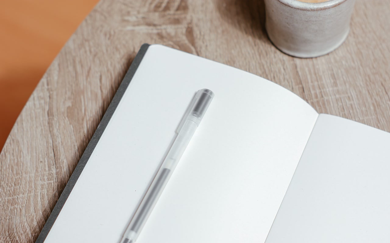 Blank open notebook with a silver pen and coffee on a wooden table