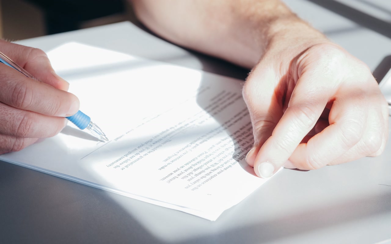 Anonymous hands signing a document with a blue pen on a desk.
