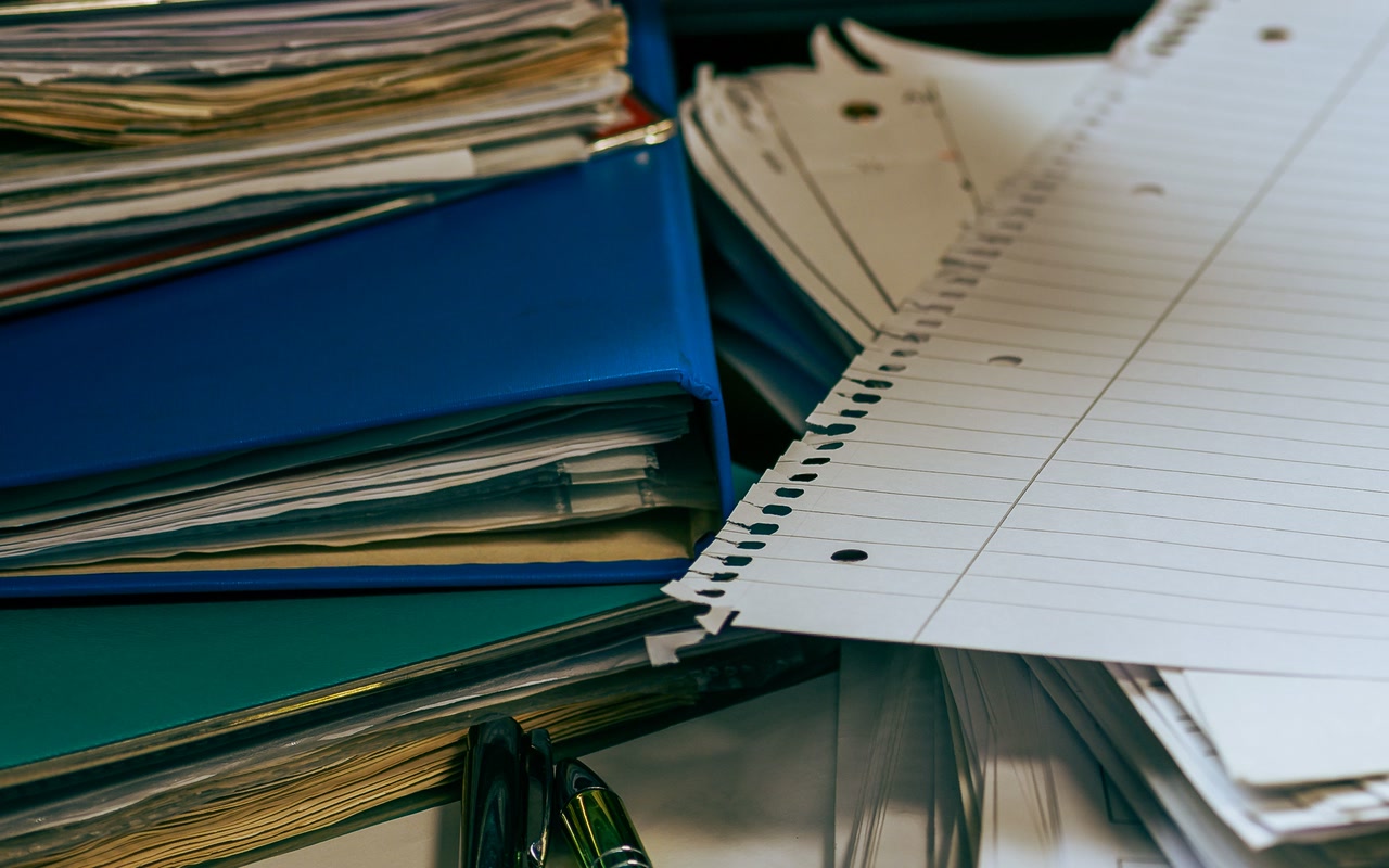 Organised office desk with stacked papers, folders, pens and a computer mouse
