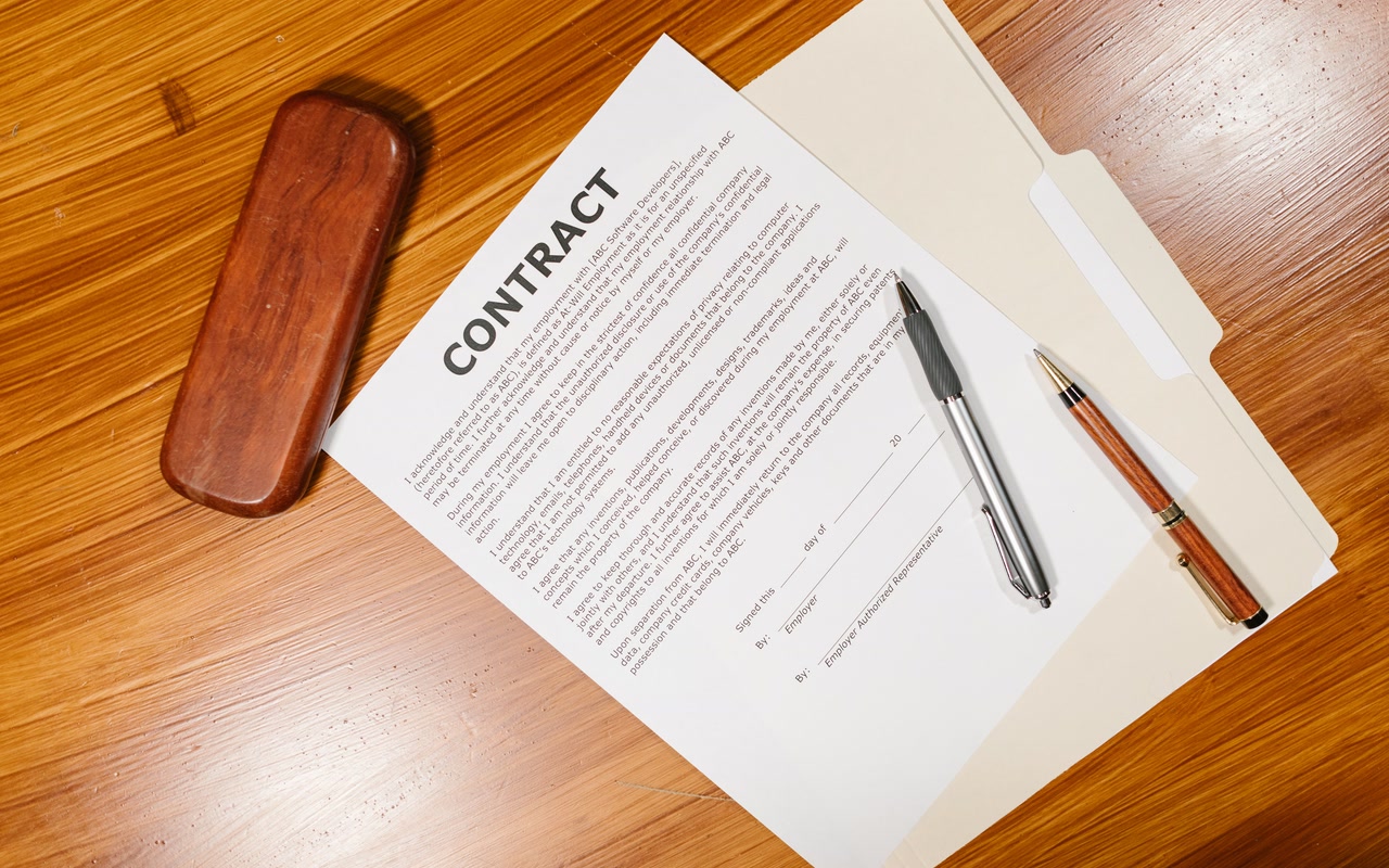 Employment agreement papers with pens and an office case arranged on a wooden desk