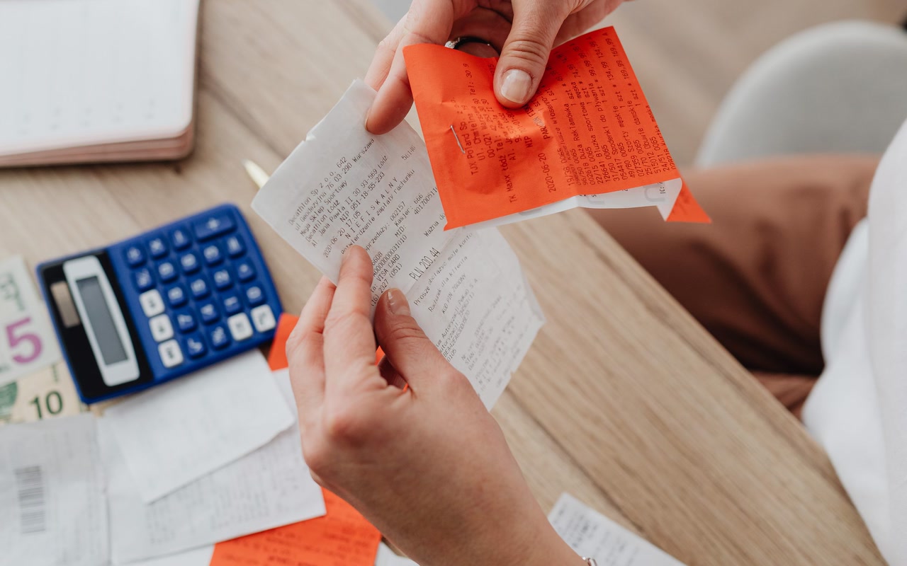 Hands organising a receipt and notes beside a calculator on a desk