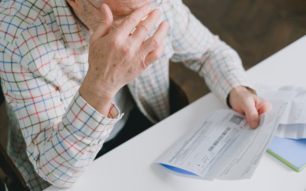 An elderly man in glasses carefully examining documents at home