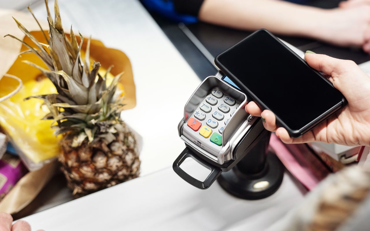 Customer holding a smartphone over a contactless payment terminal at a shop checkout