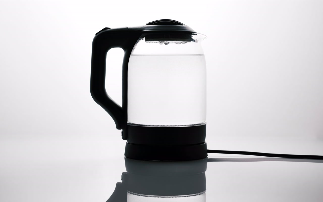 A glass electric kettle filled with water on a reflective surface