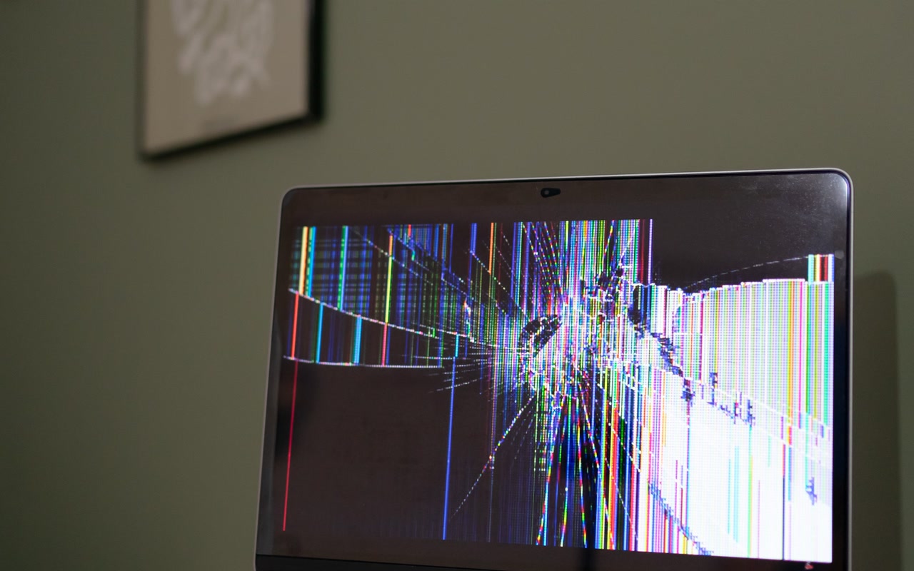A laptop with a cracked and malfunctioning screen on a desk