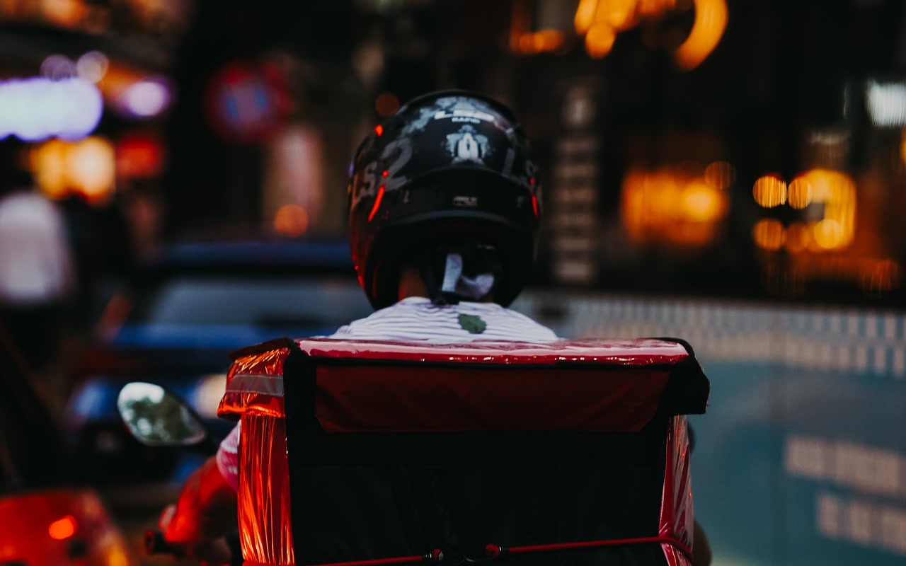Silhouetted delivery rider travelling through evening city traffic