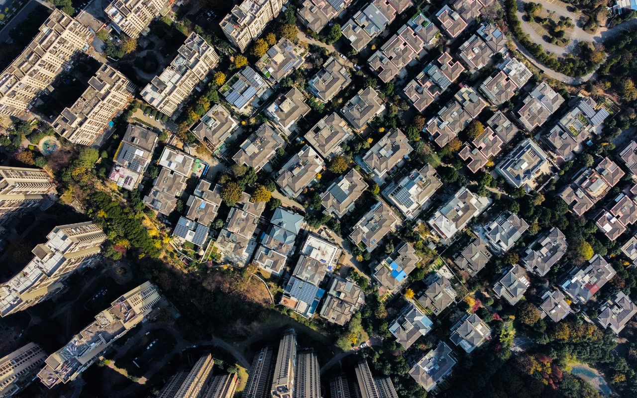Aerial daytime view of a dense residential complex, showing rows of rooftops and closely spaced apartment blocks from above