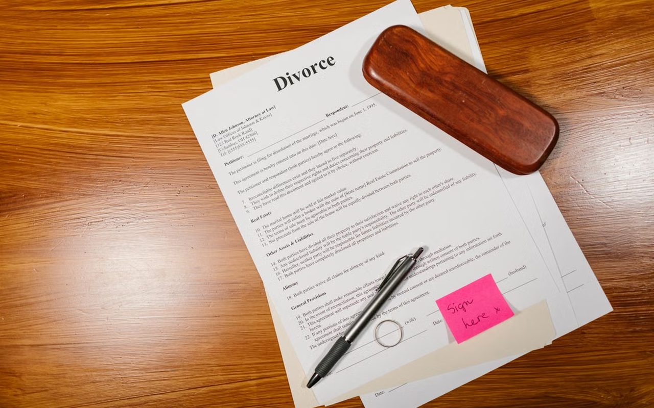 Divorce agreement papers on a wooden desk with a pen, a wedding ring and a sign-here note