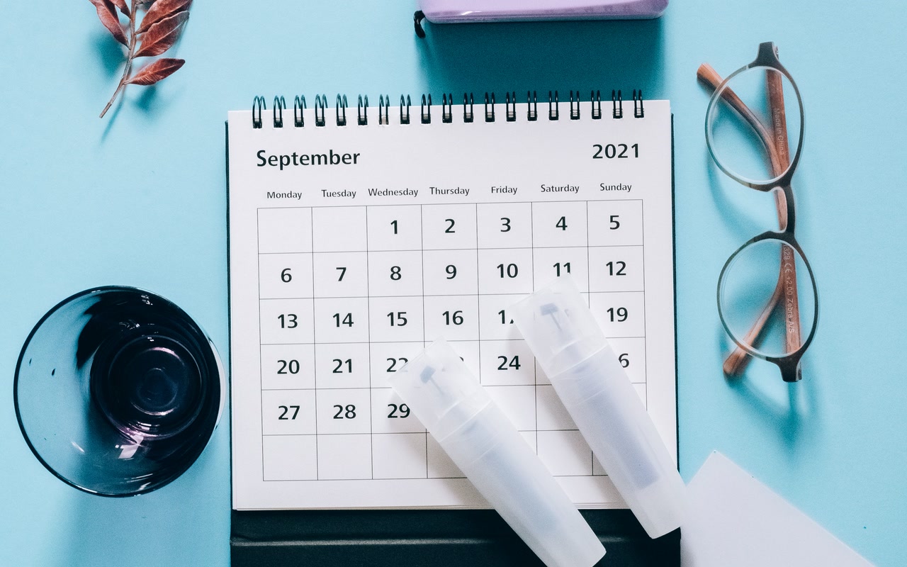 Desk calendar with glasses, camera and leaves on a blue background