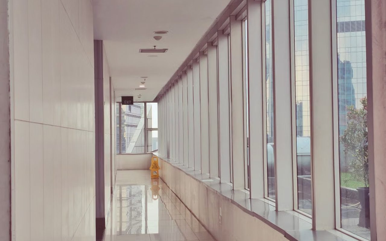 An empty office corridor with tall windows looking out on city towers