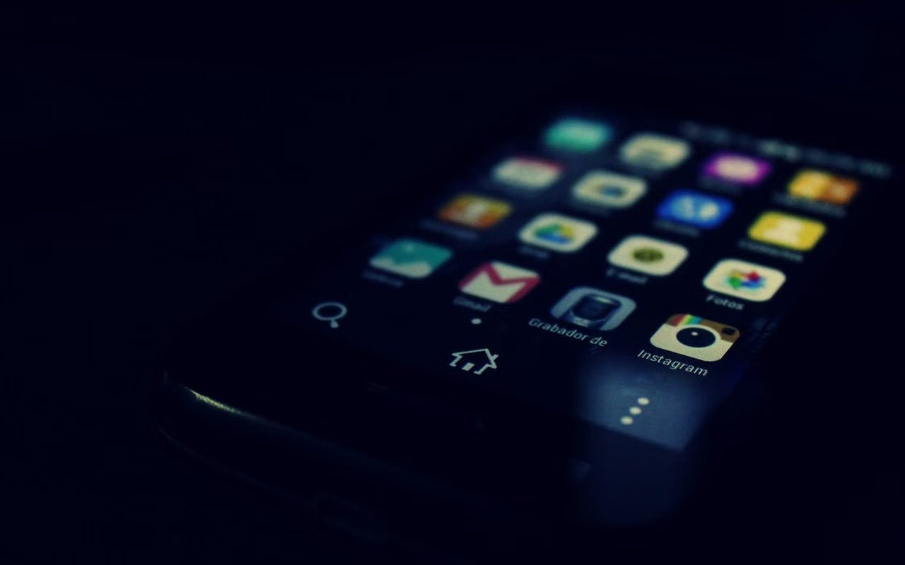 A smartphone lying face-up in a dark room, its home screen the only source of light