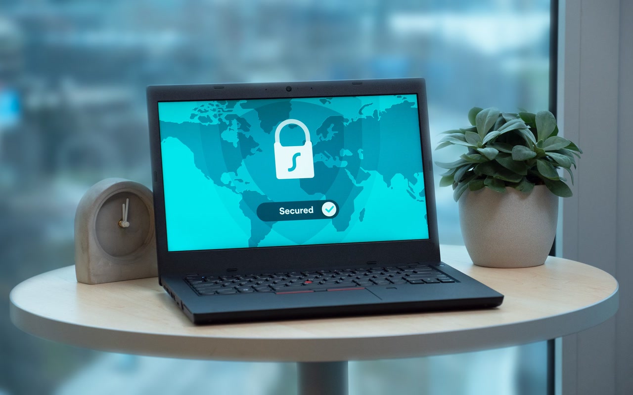 Laptop displaying a security lock icon on a round table beside a plant and clock