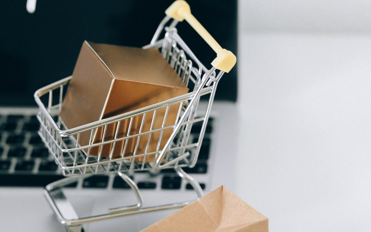 Miniature shopping cart with a small parcel resting on a laptop keyboard