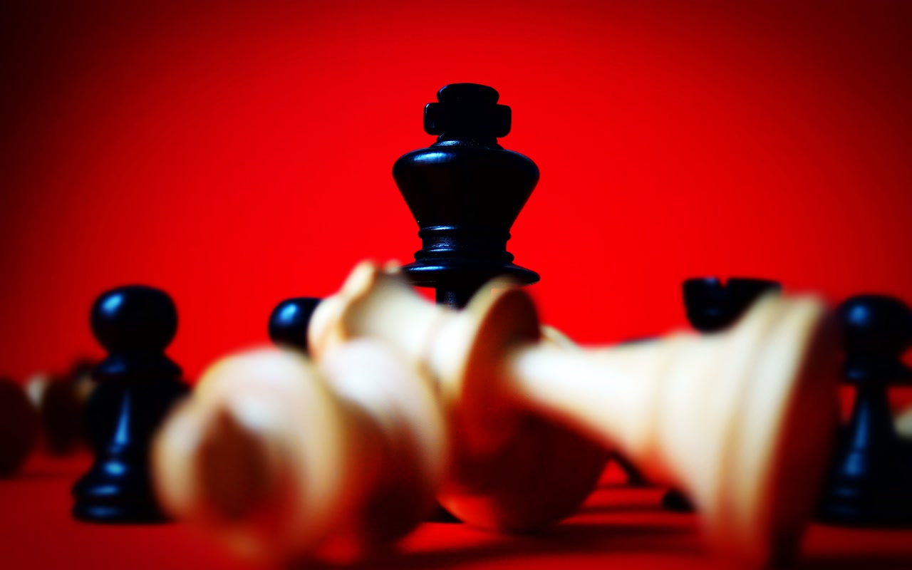 Black chess king standing among toppled pawns on a red background