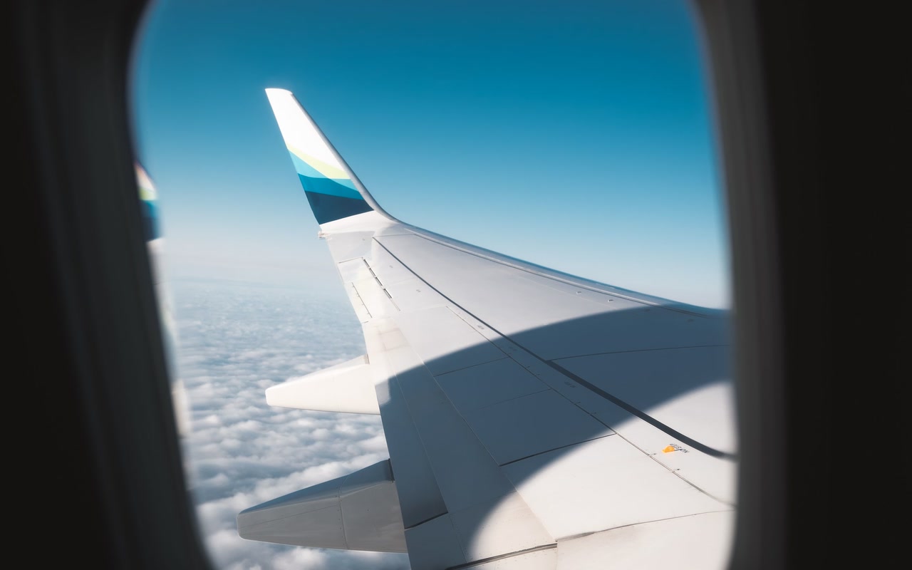 White airplane wing seen above clouds through a passenger window