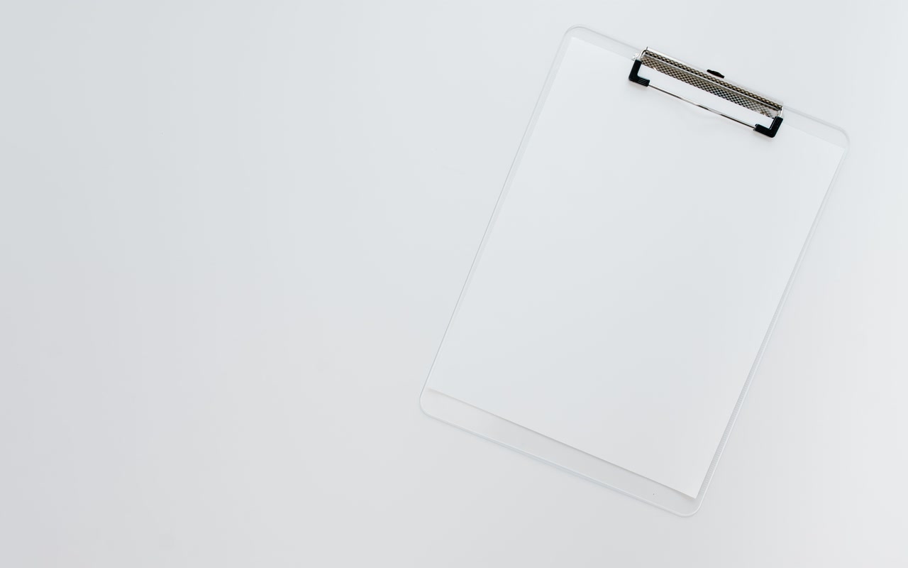 Blank white paper held by a transparent clipboard on a clean white surface