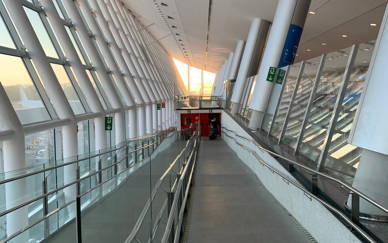 Empty modern airport terminal corridor with tall glass windows, exposed metal framing and pale reflective flooring