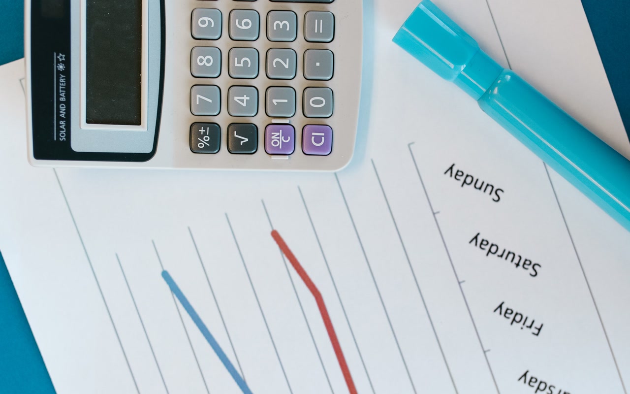 Overhead view of a calculator resting on white printed sheets beside graph paper and a turquoise marker on a desk