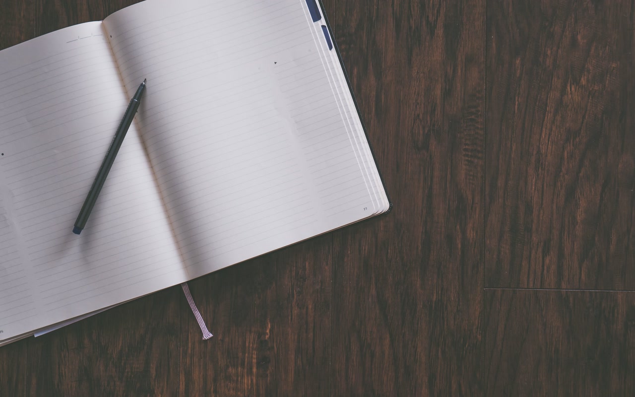 Open blank notebook with a pen resting on a wooden desk