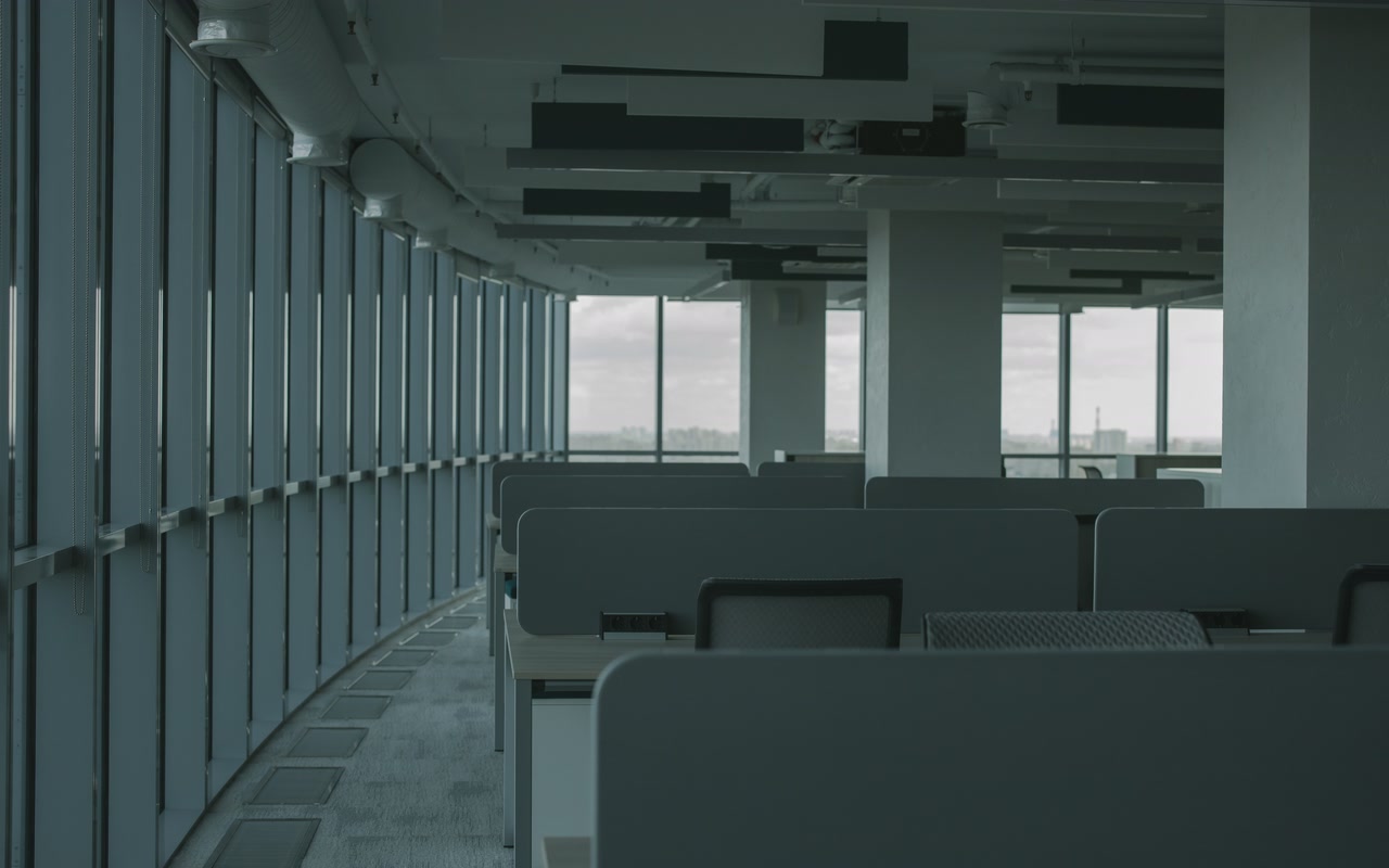 Empty modern office lounge with rows of desks and chairs beside tall windows