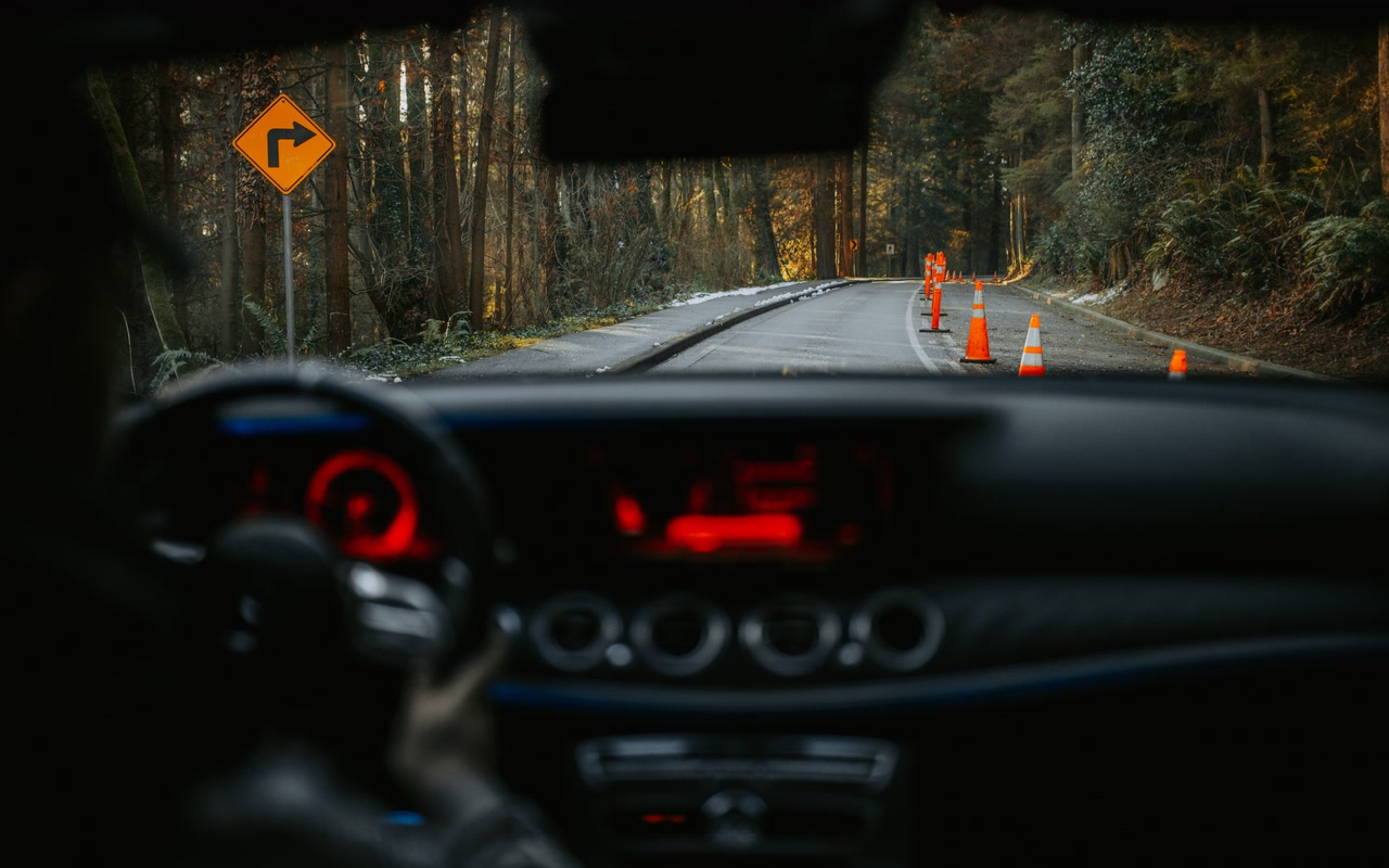 View from a car dashboard of a rural road with traffic cones and a turn sign.