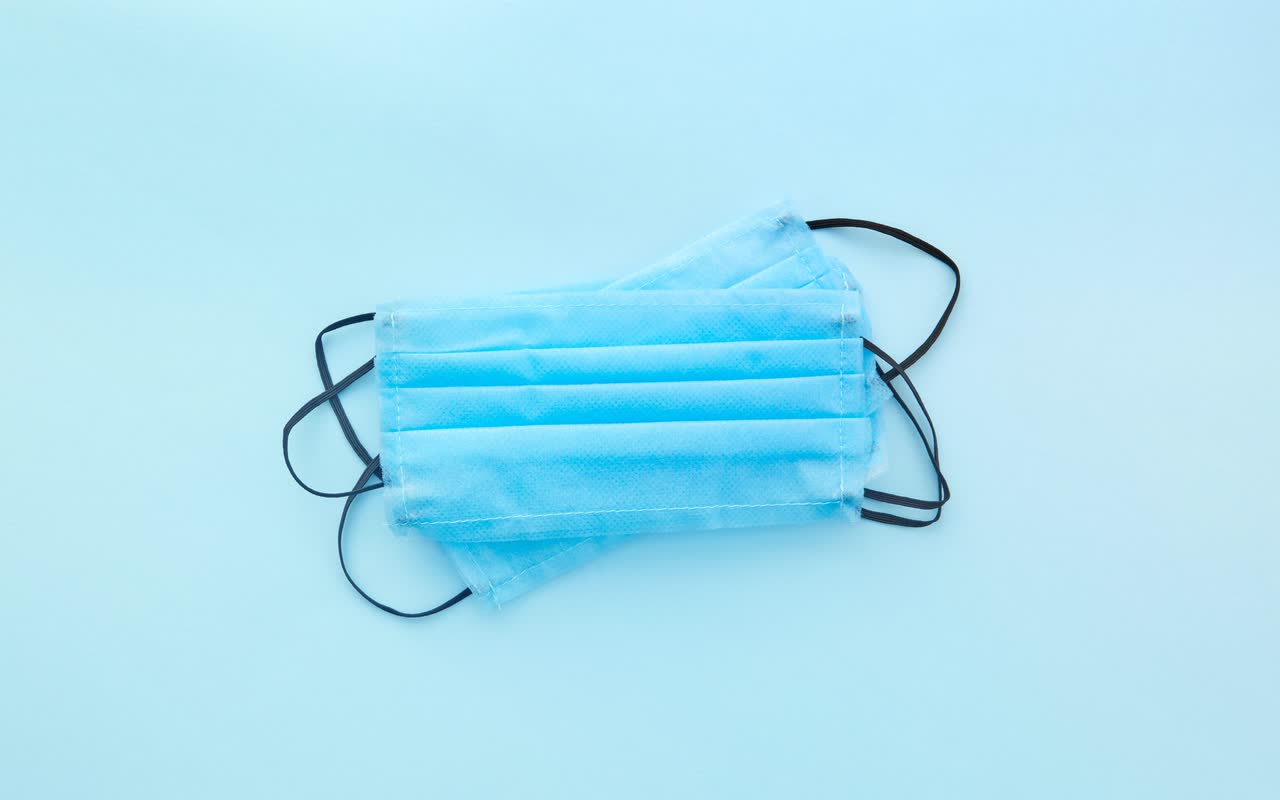 Two blue surgical face masks on a light blue background