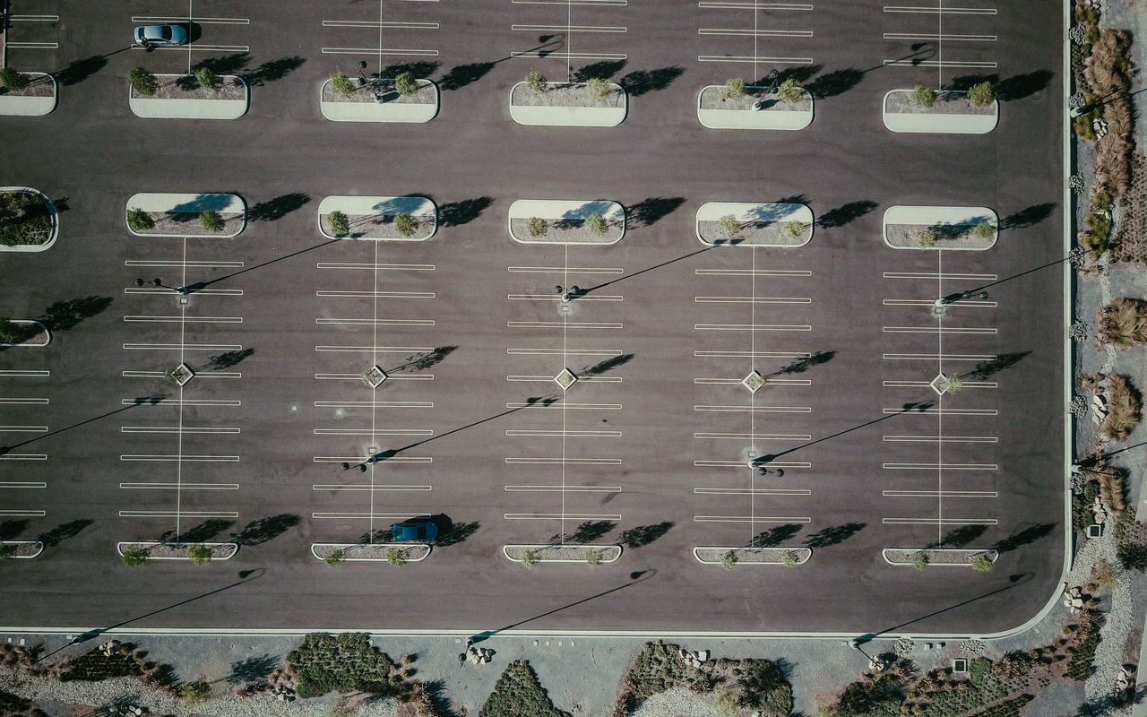 Aerial view of an empty parking lot with painted bays, trees and long shadows