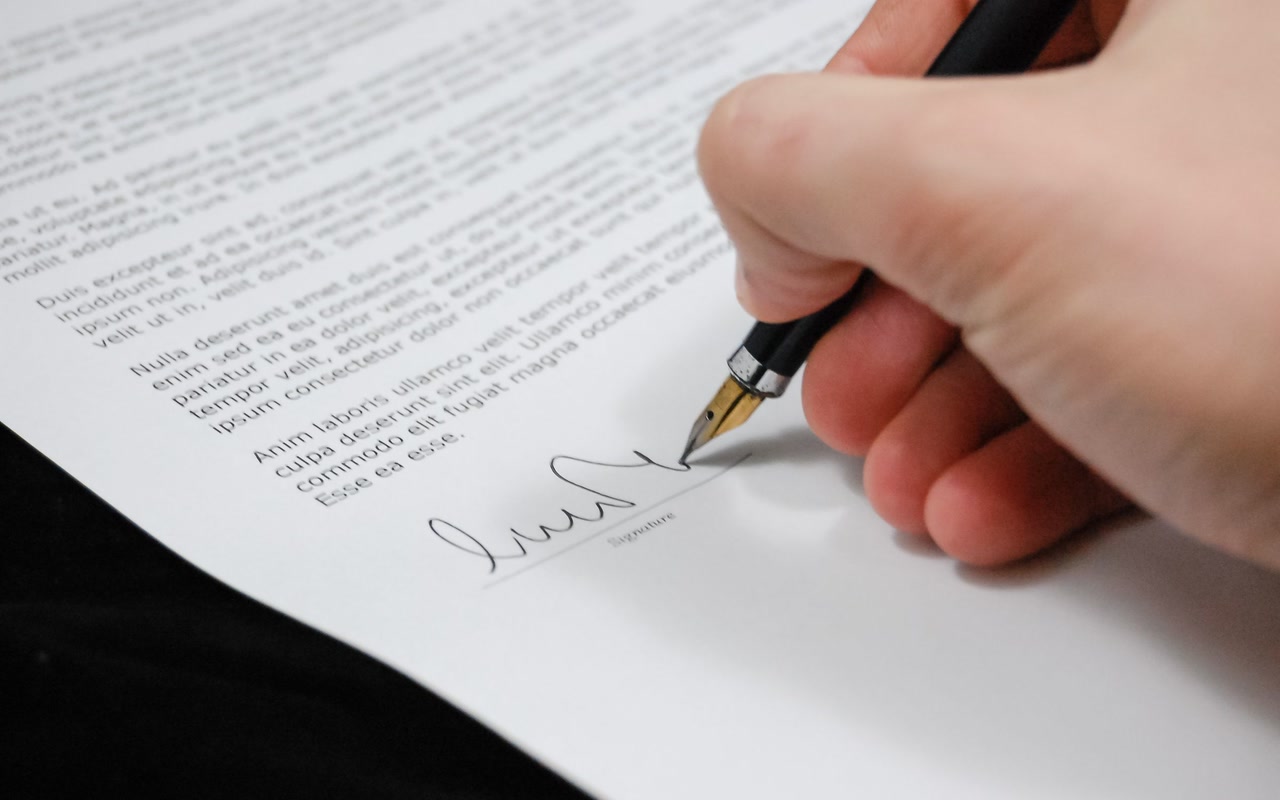 Close-up of a hand using a fountain pen to sign a document on a wooden desk