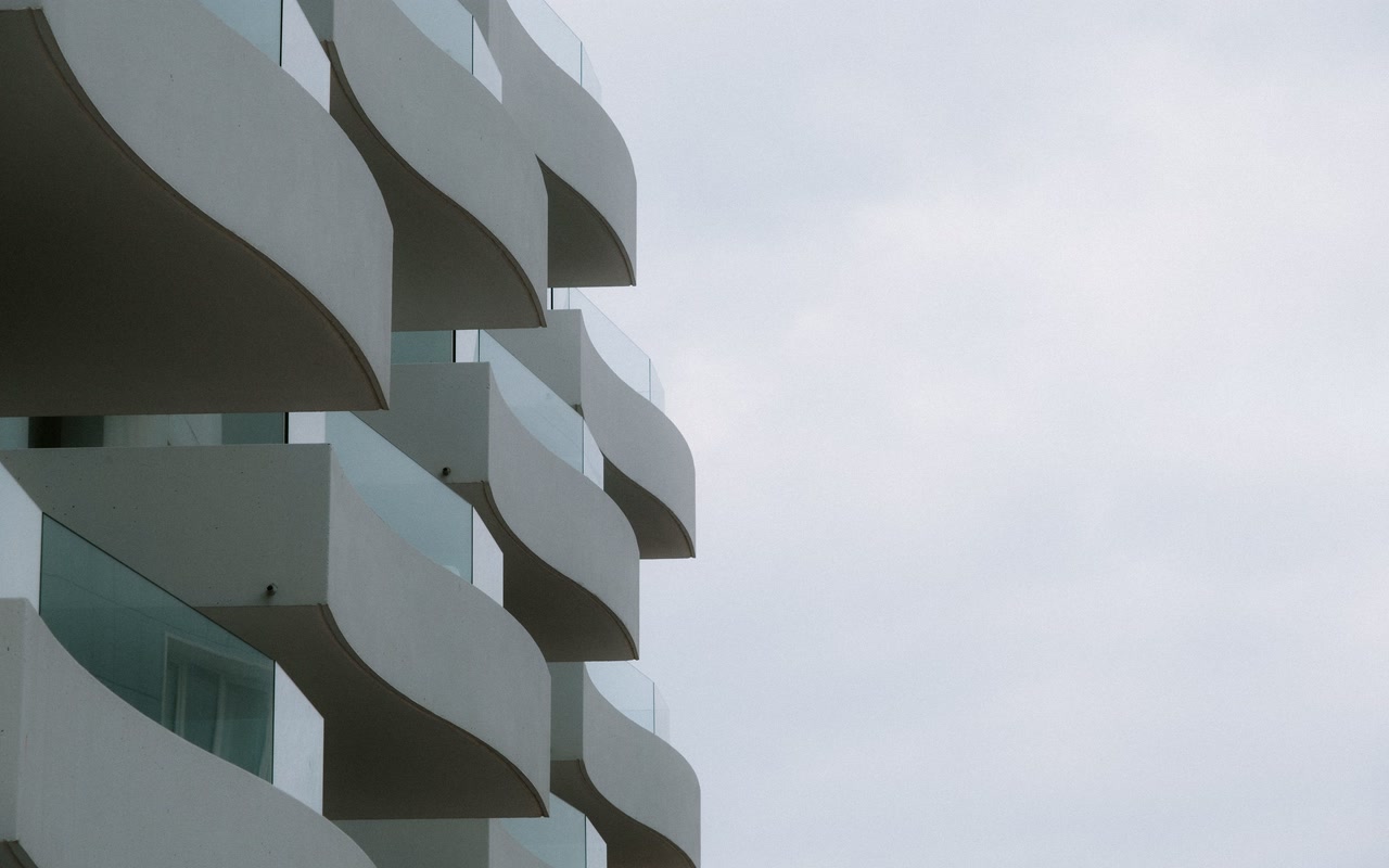 Rows of curved concrete balconies stacked across the facade of a high-rise residential building under an overcast sky.