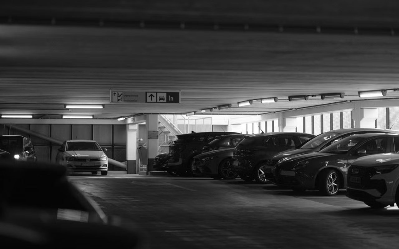 Rows of parked cars on a dim multi-storey car park deck, in black and white