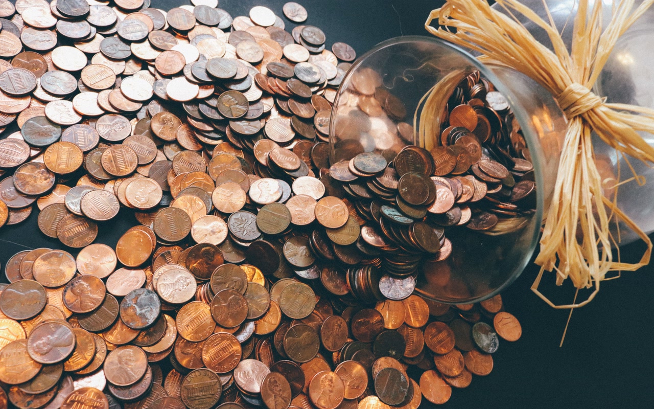 Glass jar tipped on its side with a spread of copper-coloured coins