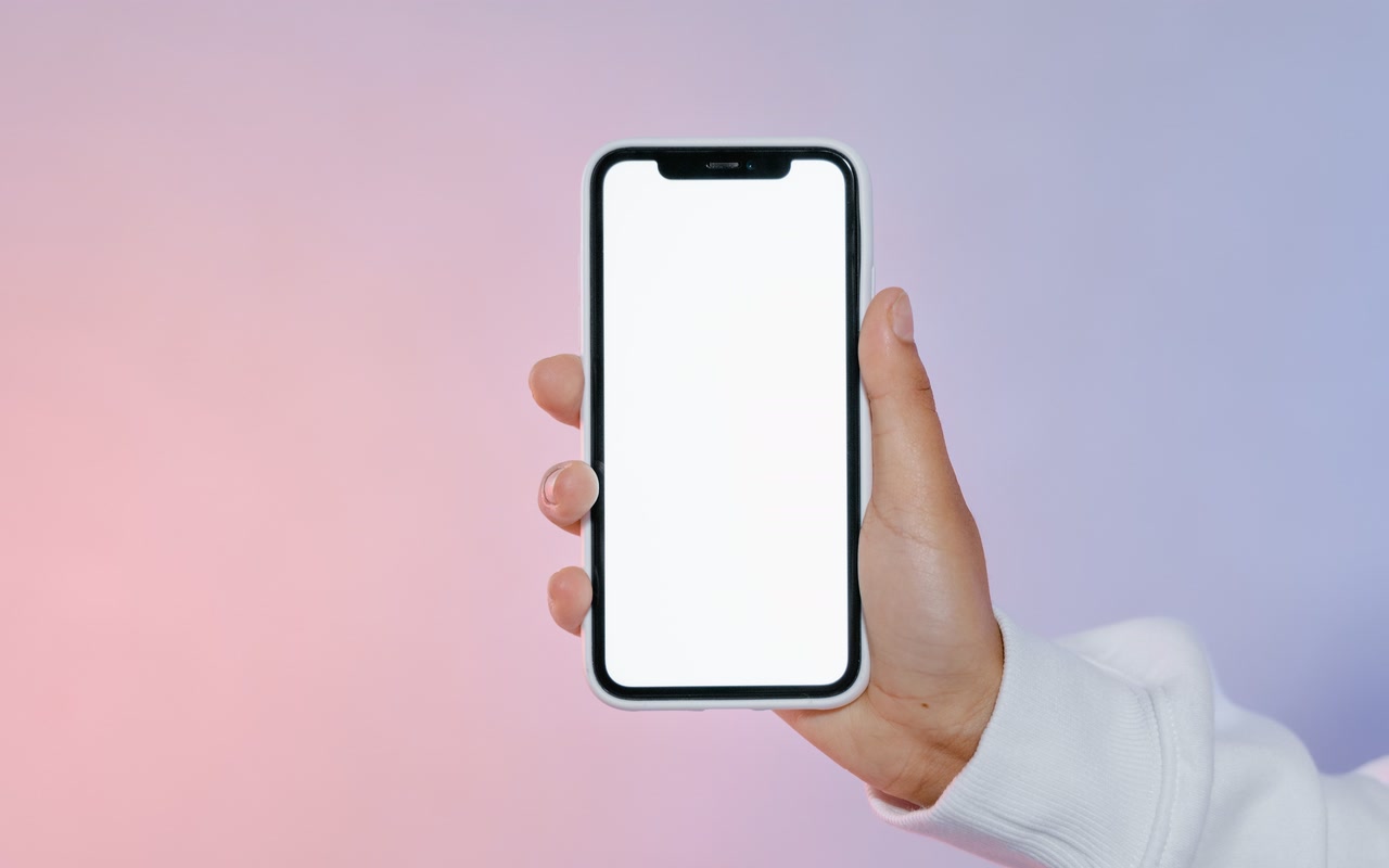 A hand in a white sleeve holding a smartphone with a blank white screen against a soft pink and blue gradient background