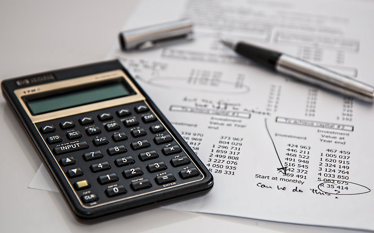A black desktop calculator and a ballpoint pen resting on white printed financial paperwork, photographed close up.