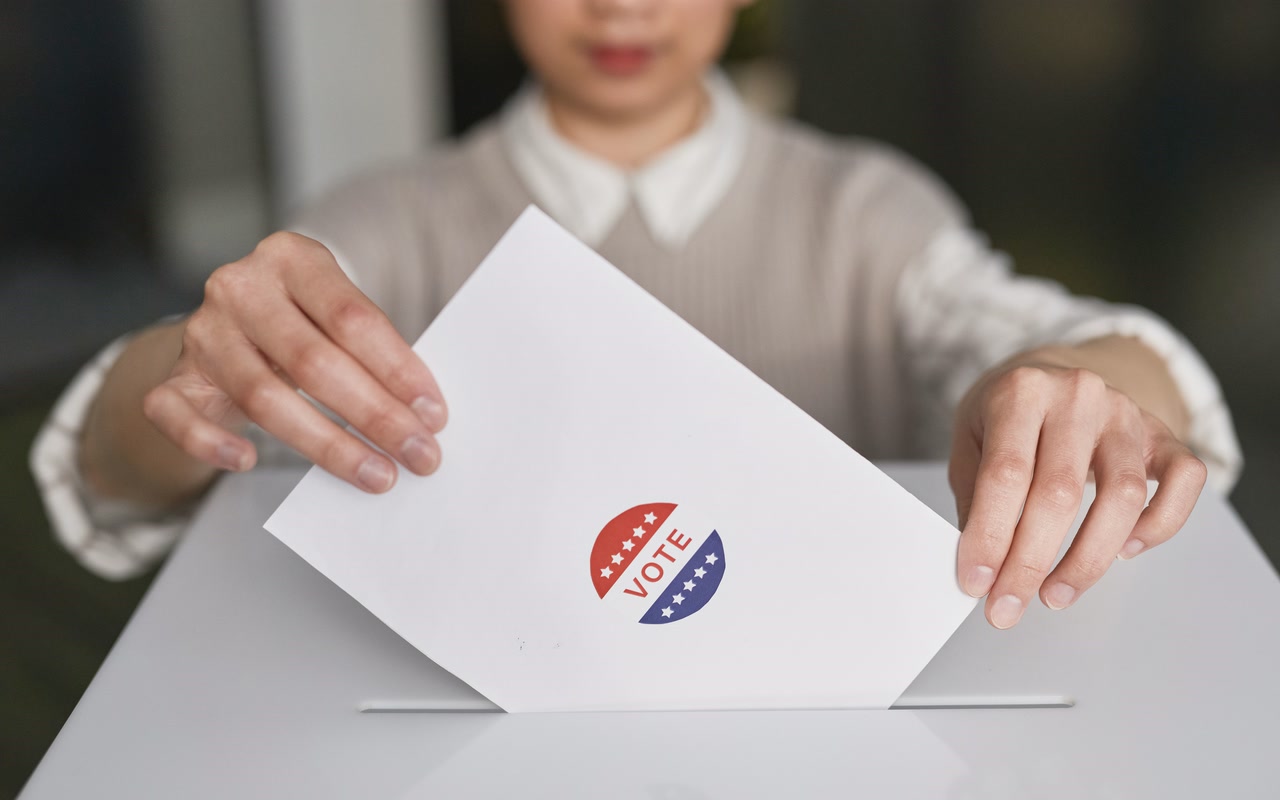 A voter placing a paper ballot into a plain ballot box